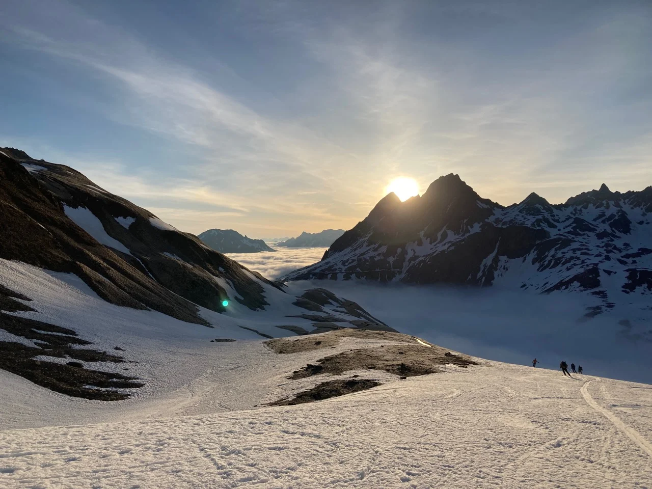 Abfahrende Skifahrer in ein nebelverhangenes Tal gegen die untergehenden Sonne | © DAV-FN / P. Schäfer