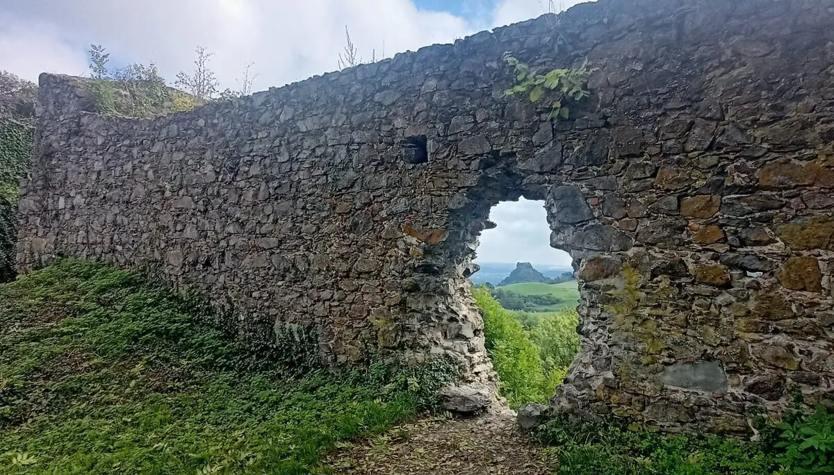 Mauerrest aus groben Steinen mit unregelmäßigem Durchbruch, dahinter grüne Landschaft und bewölkter Himmel | © DAV-FN / M. Gross