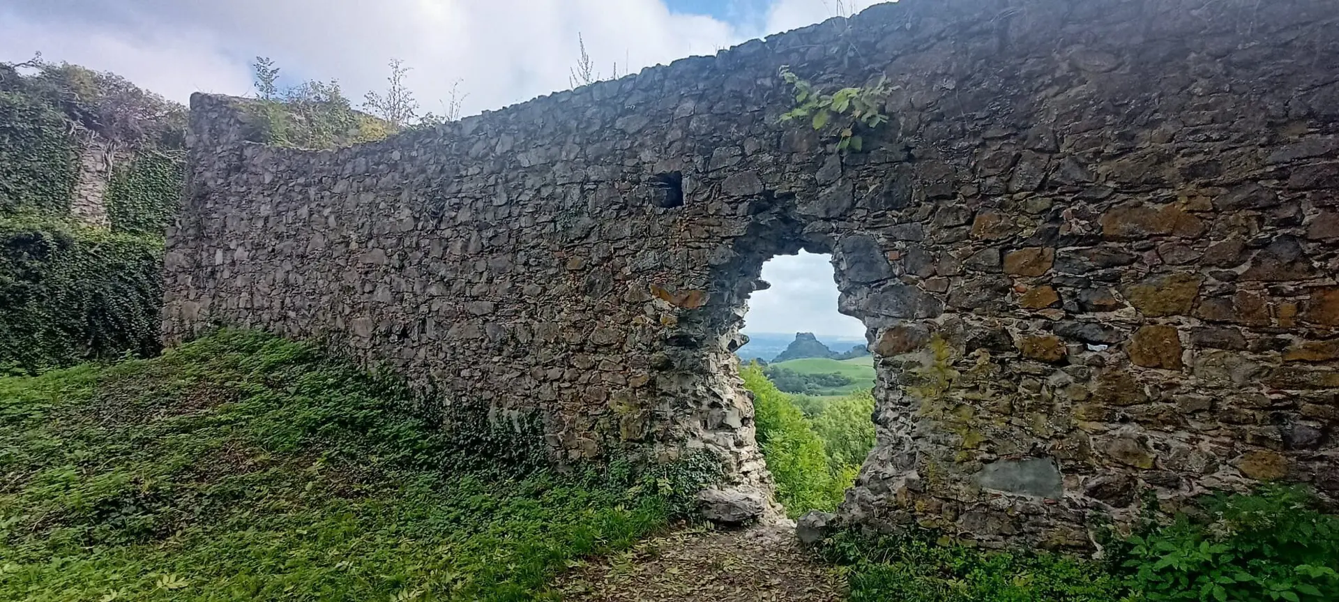 Mauerrest aus groben Steinen mit unregelmäßigem Durchbruch, dahinter grüne Landschaft und bewölkter Himmel | © DAV-FN / M. Gross