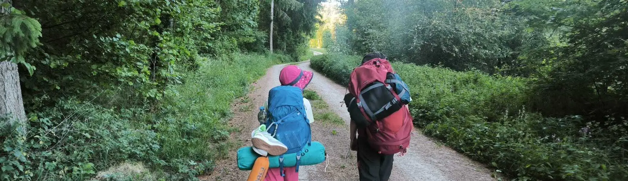 Zwei Kinder mit Rucksäcken und Campingausrüstung wandern auf einem Waldweg | © DAV-FN / M. Gross
