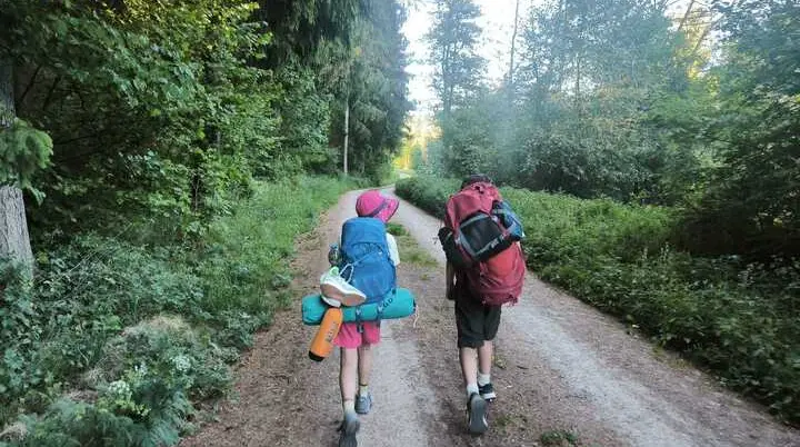 Zwei Kinder mit Rucksäcken und Campingausrüstung wandern auf einem Waldweg | © DAV-FN / M. Gross