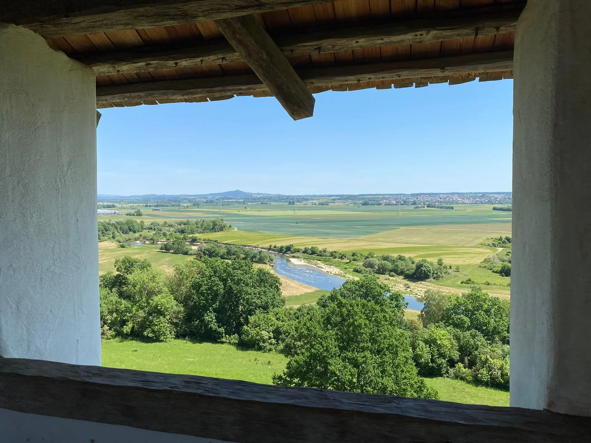 Blick aus einem Fenster mit Holzbalken auf eine Flusslandschaft mit Feldern und Bäumen unter blauem Himmel | © DAV-FN / M. Gross