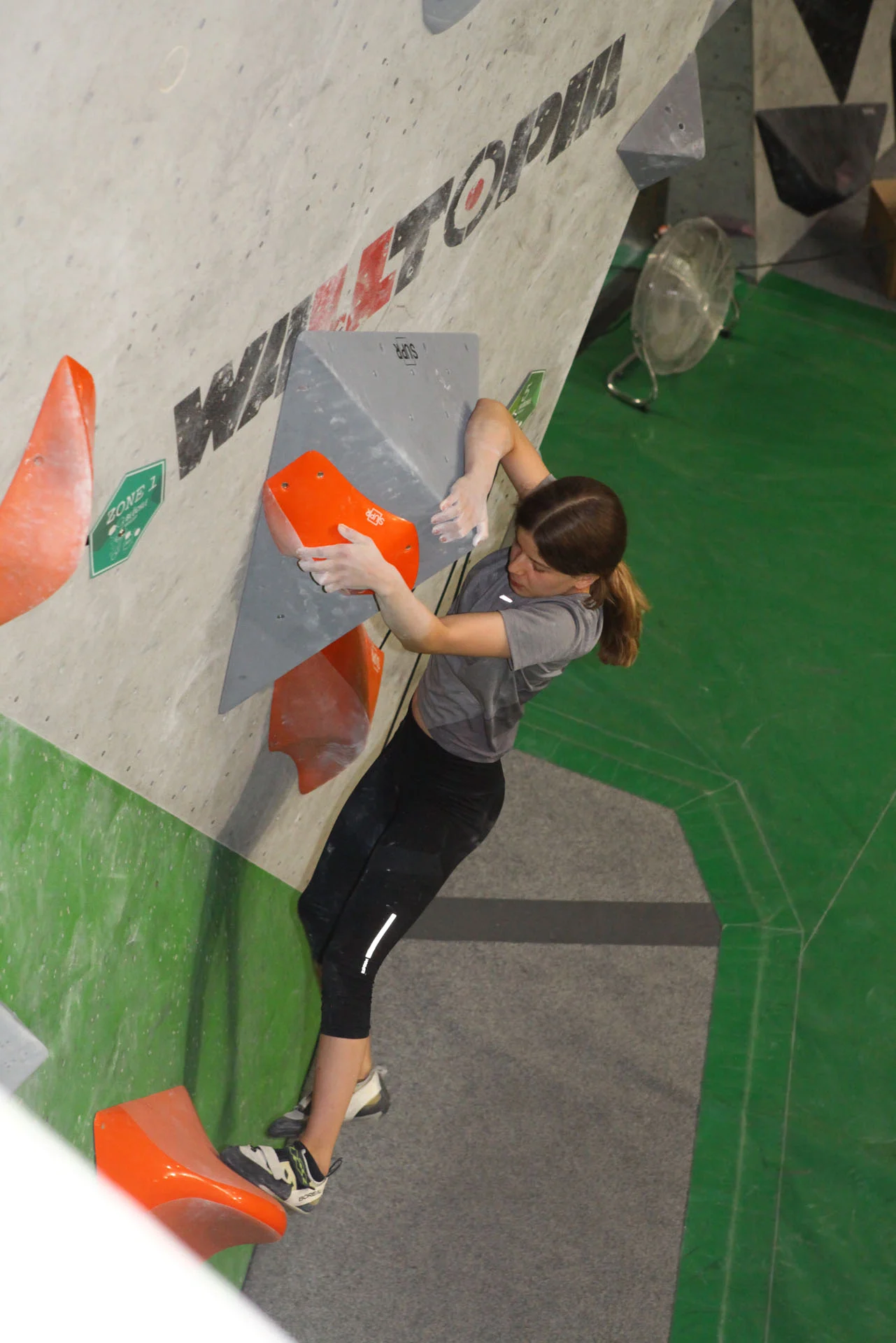 Jugendlice klettert an einer Indoor-Kletterwand und greift nach einem großen orangen Griff | © DAV-FN Thomas Müller