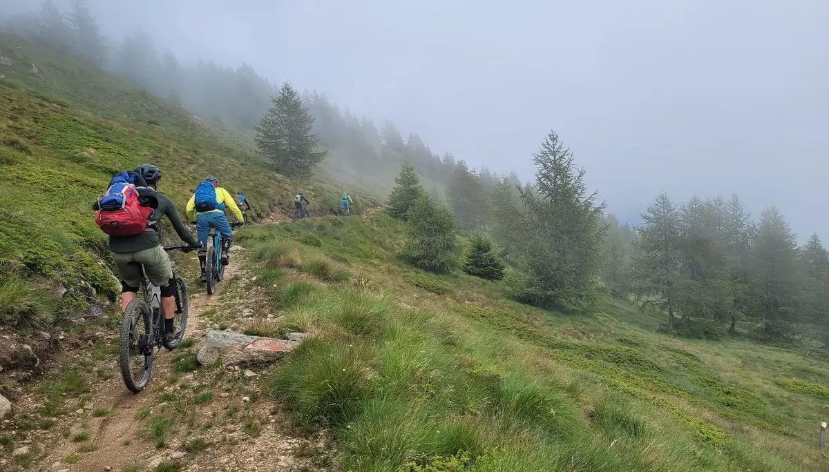 Gruppe von Mountainbikern fährt auf einem schmalen Pfad durch neblige, grüne Berglandschaft | © DAV-FN / E. Flöth, M. Arzner, S. Haberer 