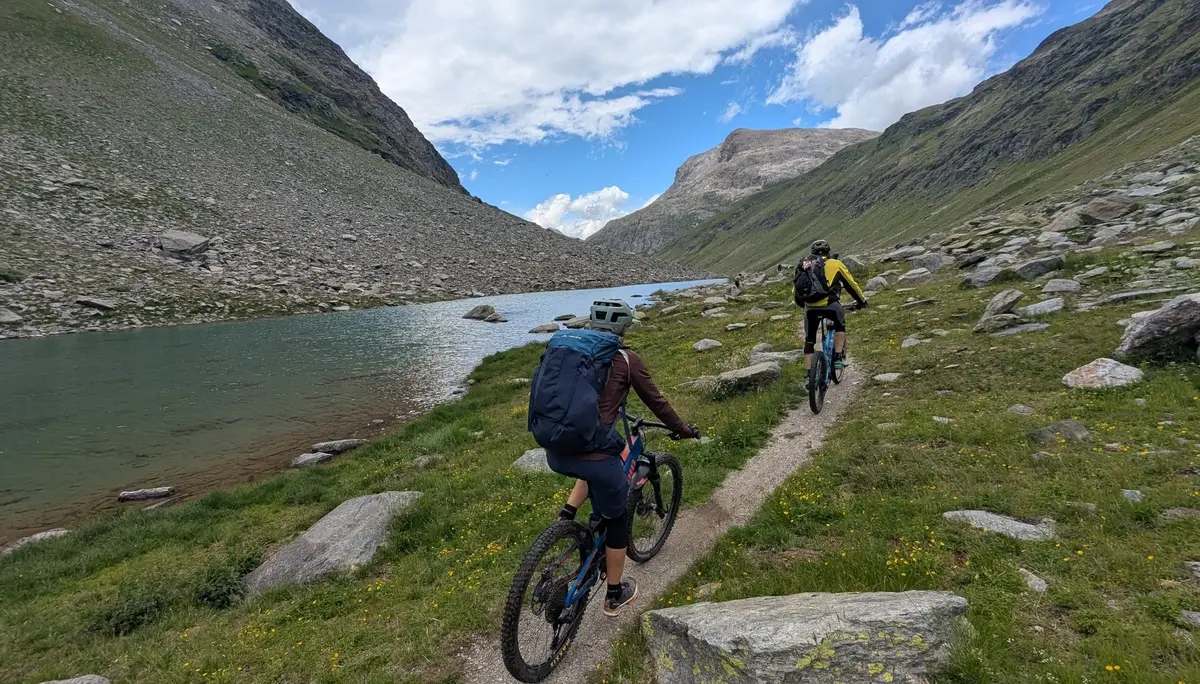 Zwei Mountainbiker fahren auf einem schmalen Pfad entlang eines Bergsees in einer alpinen Landschaft | © DAV-FN / E. Flöth, M. Arzner, S. Haberer 
