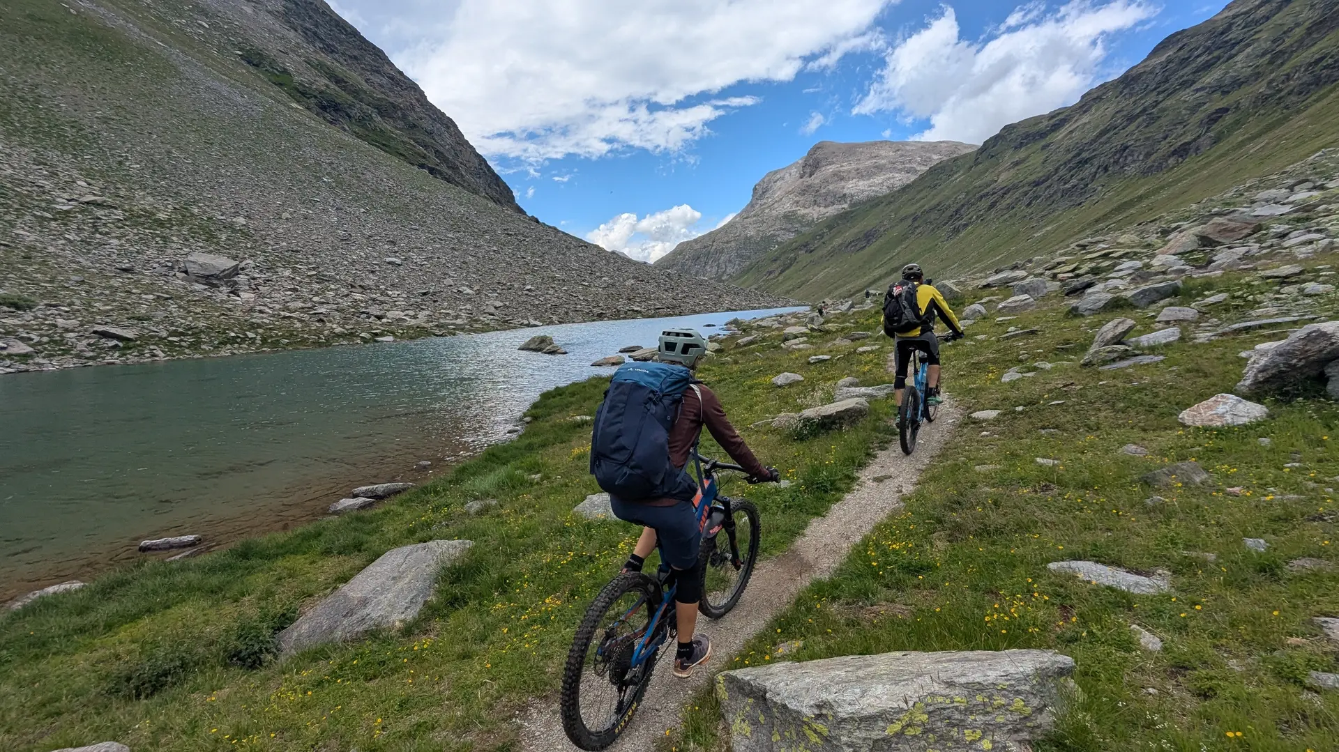 Zwei Mountainbiker fahren auf einem schmalen Pfad entlang eines Bergsees in einer alpinen Landschaft | © DAV-FN / E. Flöth, M. Arzner, S. Haberer 
