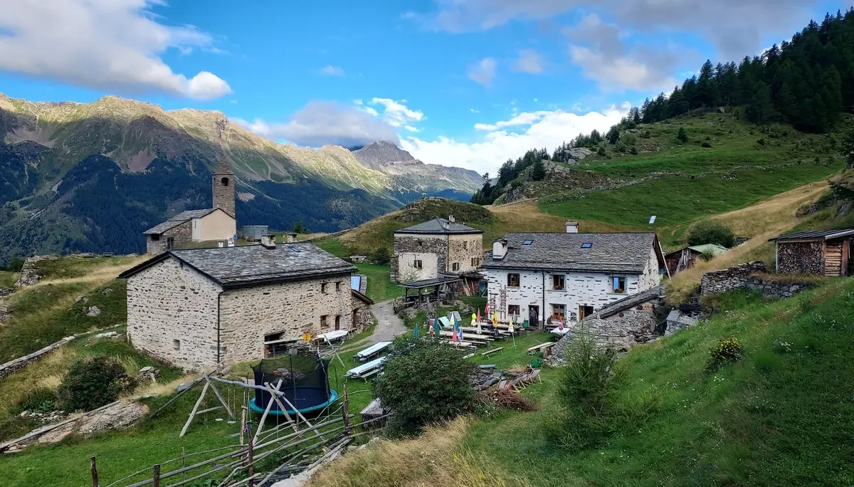 Bergdorf mit mehreren Steinhäusern und einer kleinen Kirche in einer grünen Berglandschaft unter blauem Himmel | © DAV-FN / E. Flöth, M. Arzner, S. Haberer 