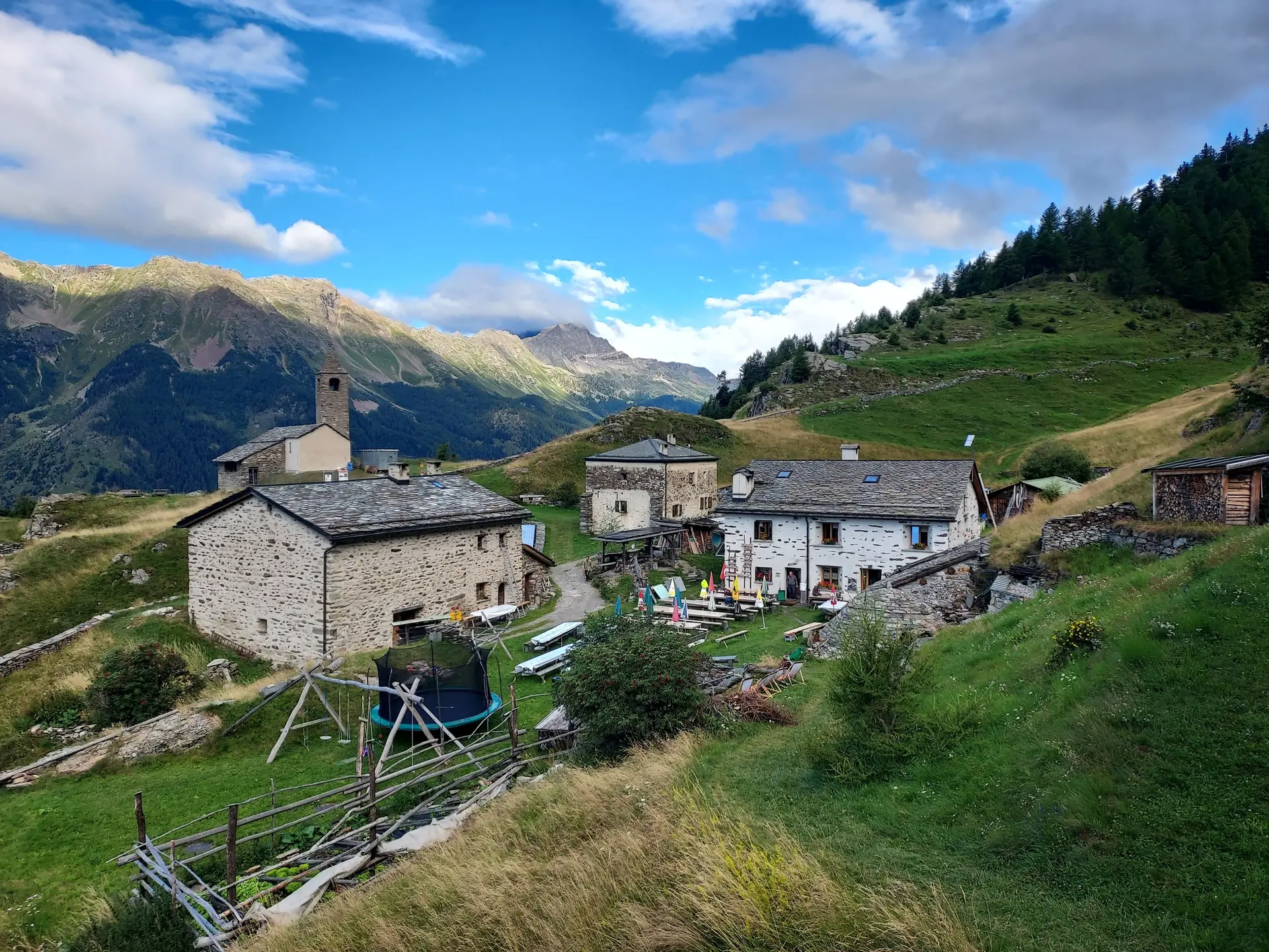 Bergdorf mit mehreren Steinhäusern und einer kleinen Kirche in einer grünen Berglandschaft unter blauem Himmel | © DAV-FN / E. Flöth, M. Arzner, S. Haberer 
