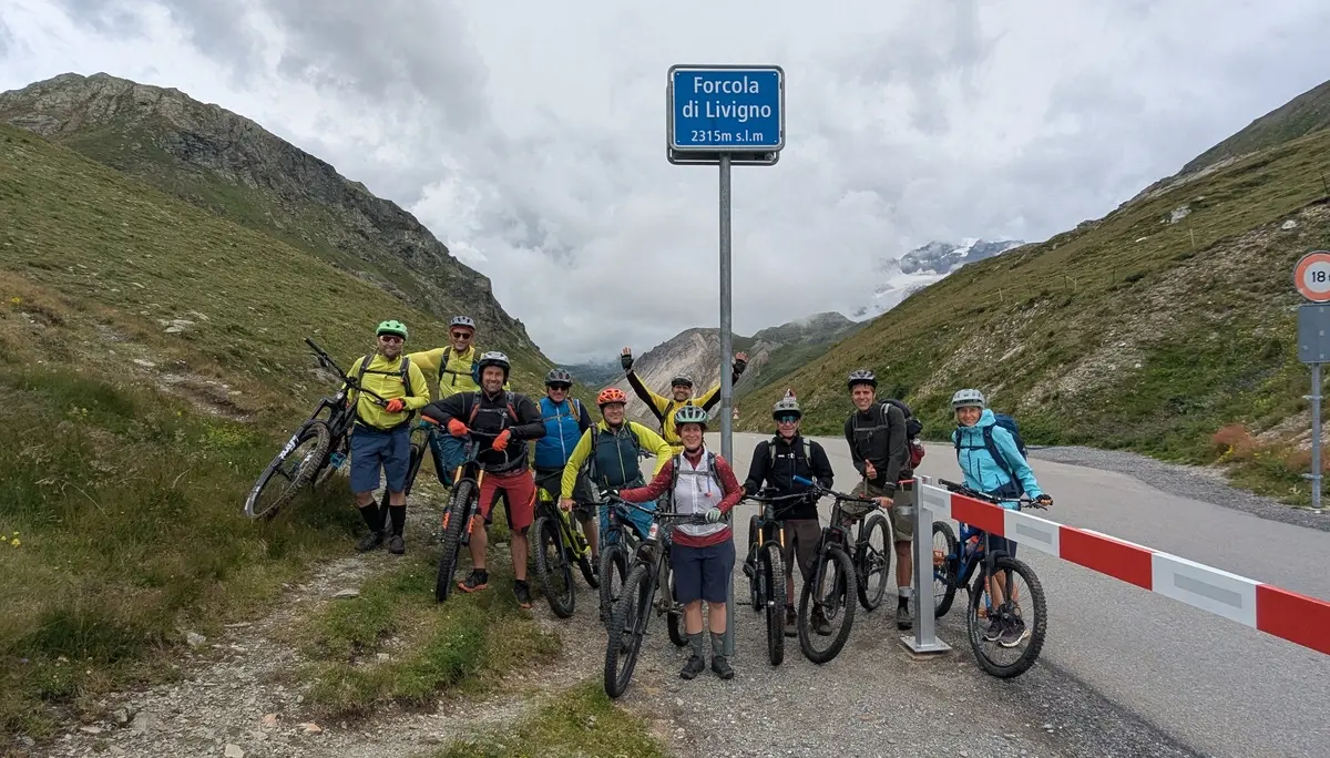 Gruppe von Mountainbikern mit Helmen und Fahrrädern steht an einem Passschild auf einer Bergstraße zwischen grünen Hängen | © DAV-FN / E. Flöth, M. Arzner, S. Haberer 