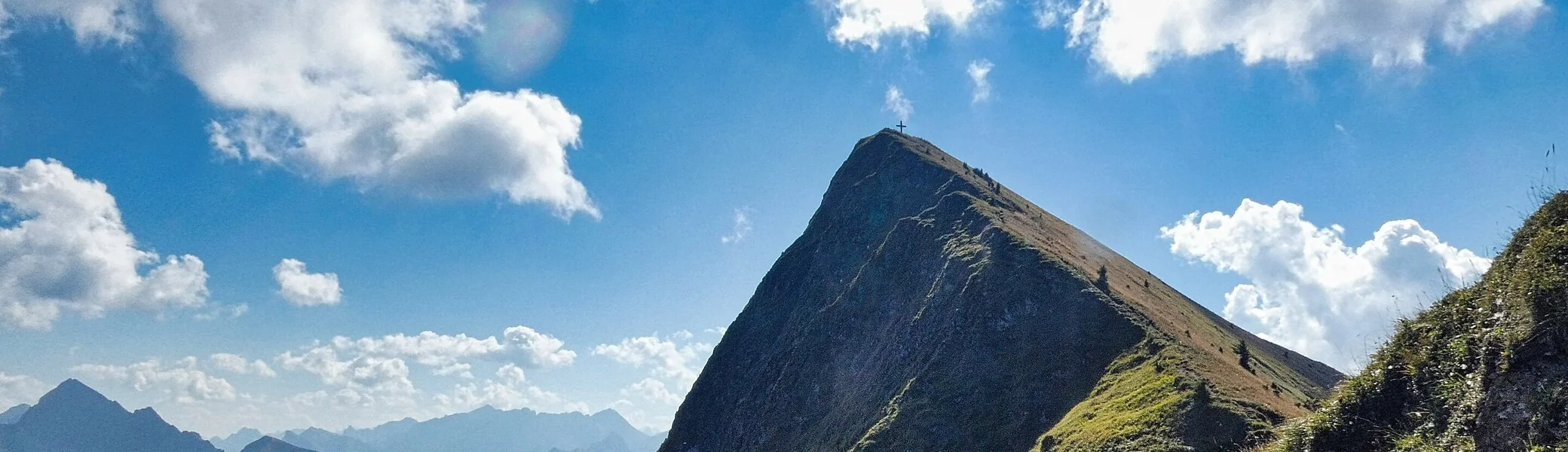 Gipfel des Glatthorn im Bregenzerwaldgebirge mit Kreuz auf dem höchsten Punkt und umliegenden Bergen unter bewölktem Himmel | © Von Steffen 962 - Eigenes Werk, CC BY-SA 4.0, auf Wikipedia