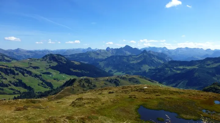 Berglandschaft mit grasbewachsenen Hügeln, kleinen Wasserflächen und dahinter mehreren Bergketten unter blauem Himmel mit wenigen Wolken | © Von Reinhard Müller - Eigenes Werk, CC BY-SA 4.0, httpscommons.wikimedia.orgwindex.phpcurid=43196985