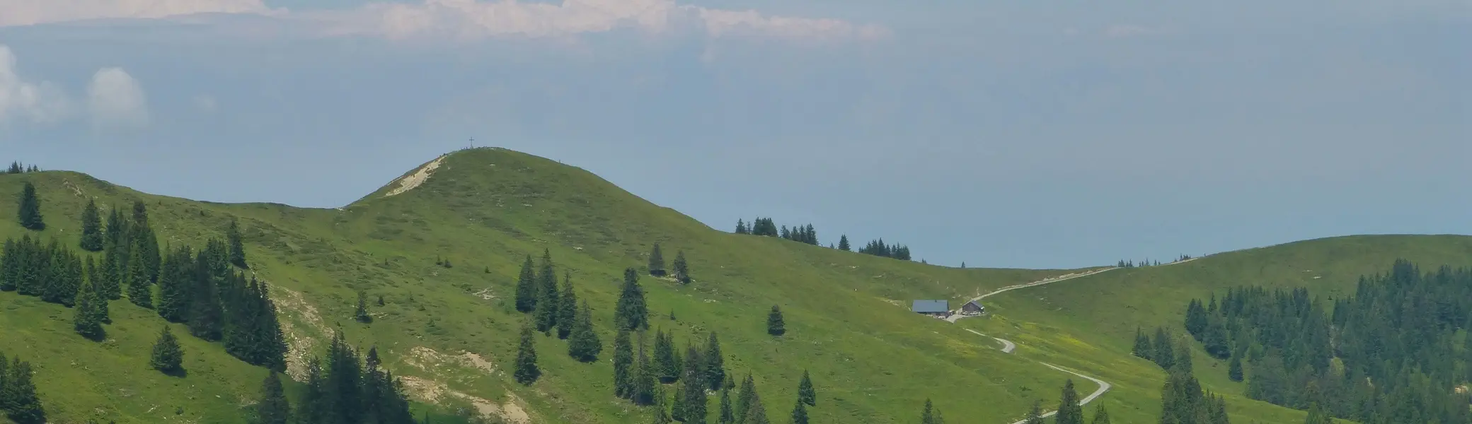 Grüne Berglandschaft mit Nadelbäumen und einem gewundenen Pfad unter blauem Himmel mit wenigen Wolken | © Von Reinhard Müller - Eigenes Werk, CC BY-SA 3.0, https://commons.wikimedia.org/w/index.php?curid=33481654