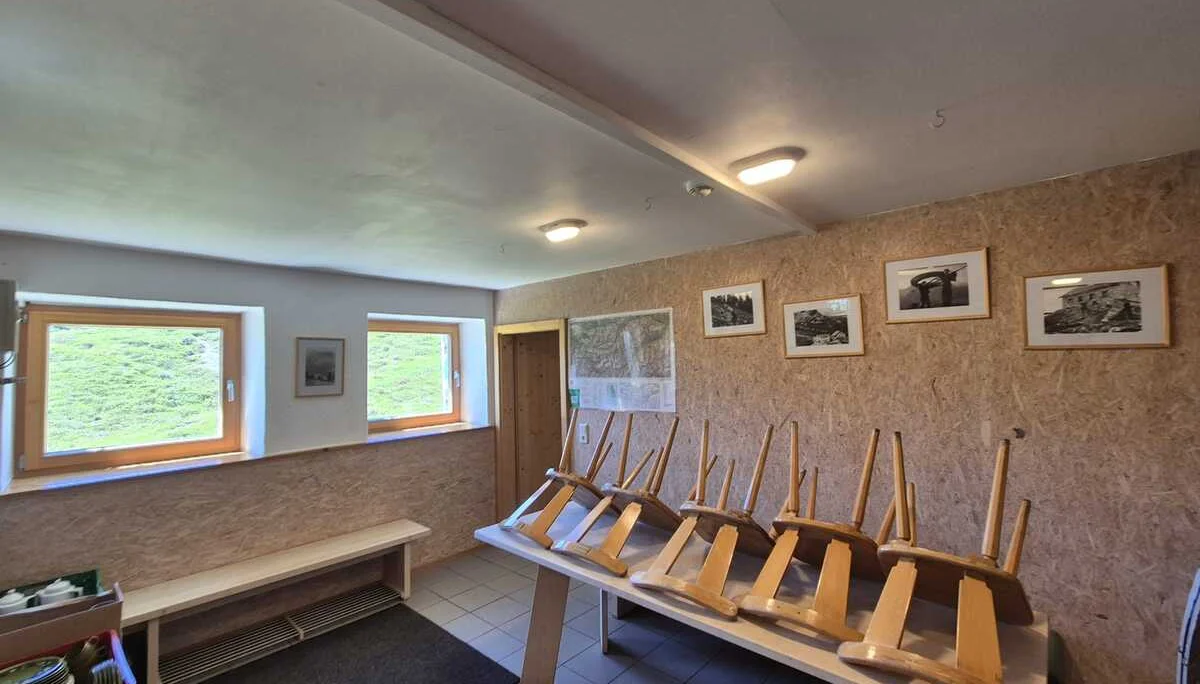 Winterraum mit umgedrehten Holzstühlen auf einem Tisch, zwei kleinen Fenstern und gerahmten Bildern an der Wand | © DAV-FN / R. Klees o. R. Zahner