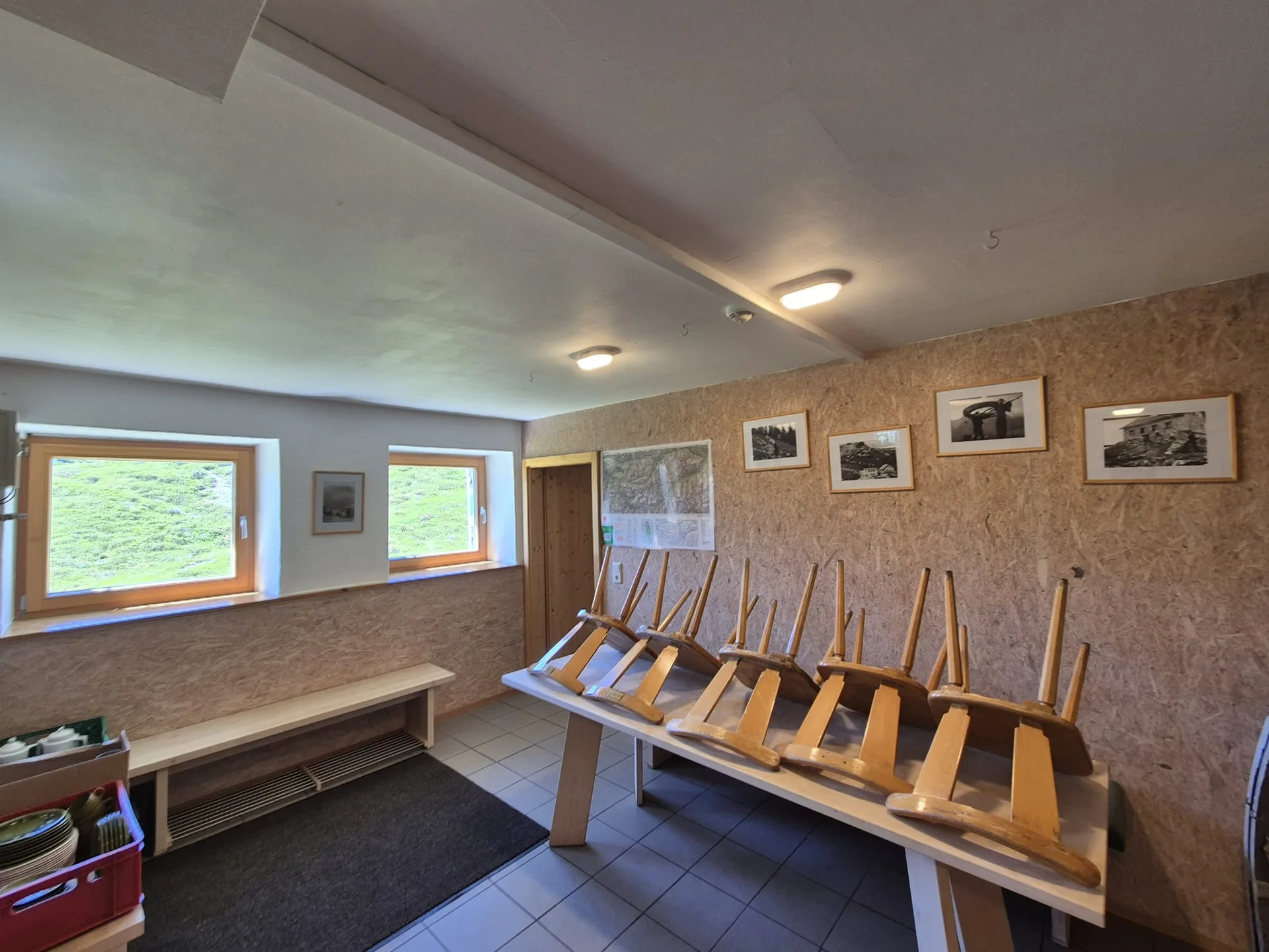 Winterraum mit umgedrehten Holzstühlen auf einem Tisch, zwei kleinen Fenstern und gerahmten Bildern an der Wand | © DAV-FN / R. Klees o. R. Zahner