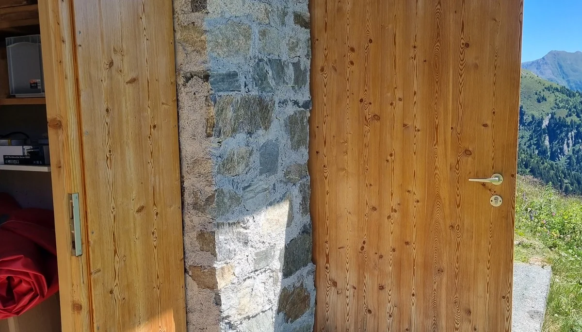 Zwei geöffnete Holztüren an der Häfler Hütte mit Berglandschaft im Hintergrund | © DAV-FN / R. Klees o. R. Zahner