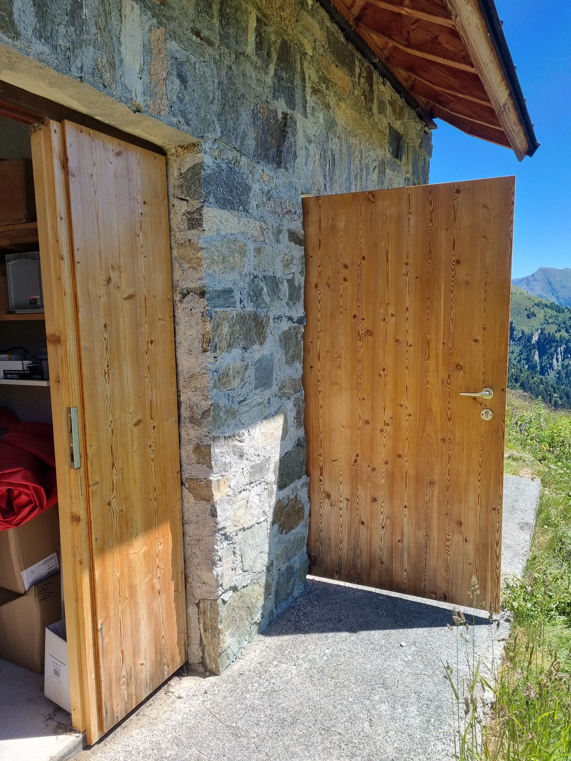 Zwei geöffnete Holztüren an der Häfler Hütte mit Berglandschaft im Hintergrund | © DAV-FN / R. Klees o. R. Zahner
