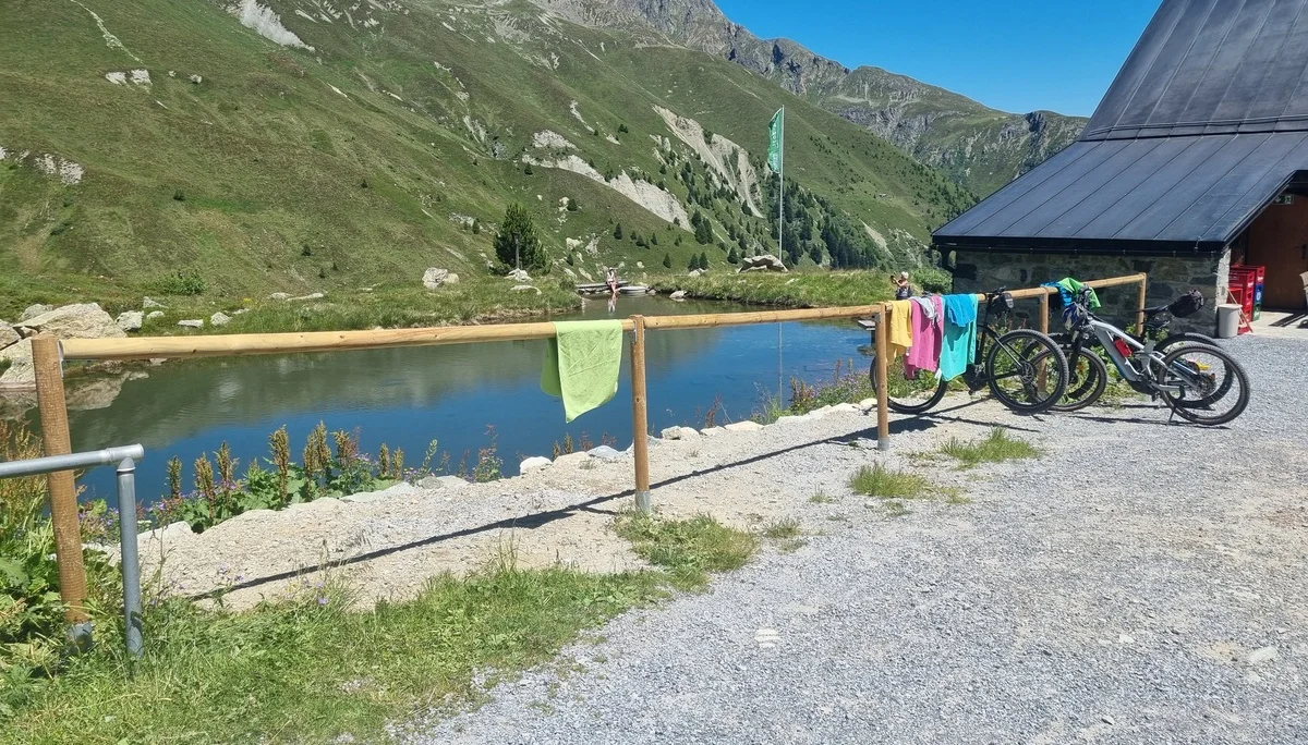 Bergsee mit grünen Hängen, Holzgeländer als MTB-Ständer mit bunten Handtüchern, zwei Mountainbikes neben der Häfler Hütte | © DAV-FN / R. Klees o. R. Zahner