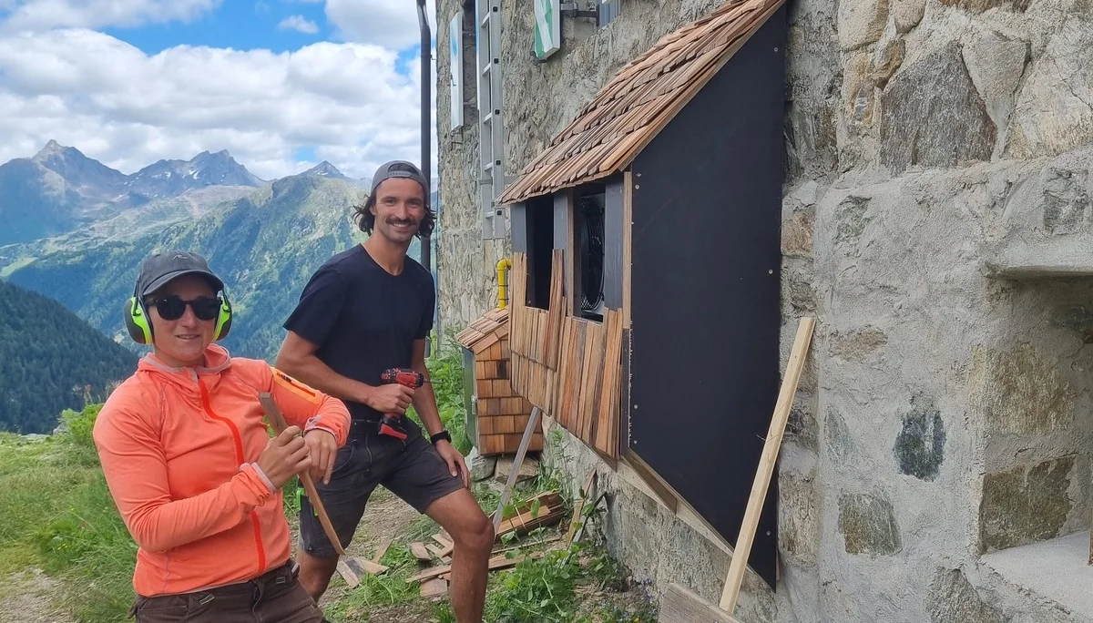 Zwei Personen arbeiten an einer Holzverkleidung an der Aussenwnd der Häfler Hütte, umgeben von Werkzeug und Holzlatten. | © DAV-FN / R. Klees o. R. Zahner