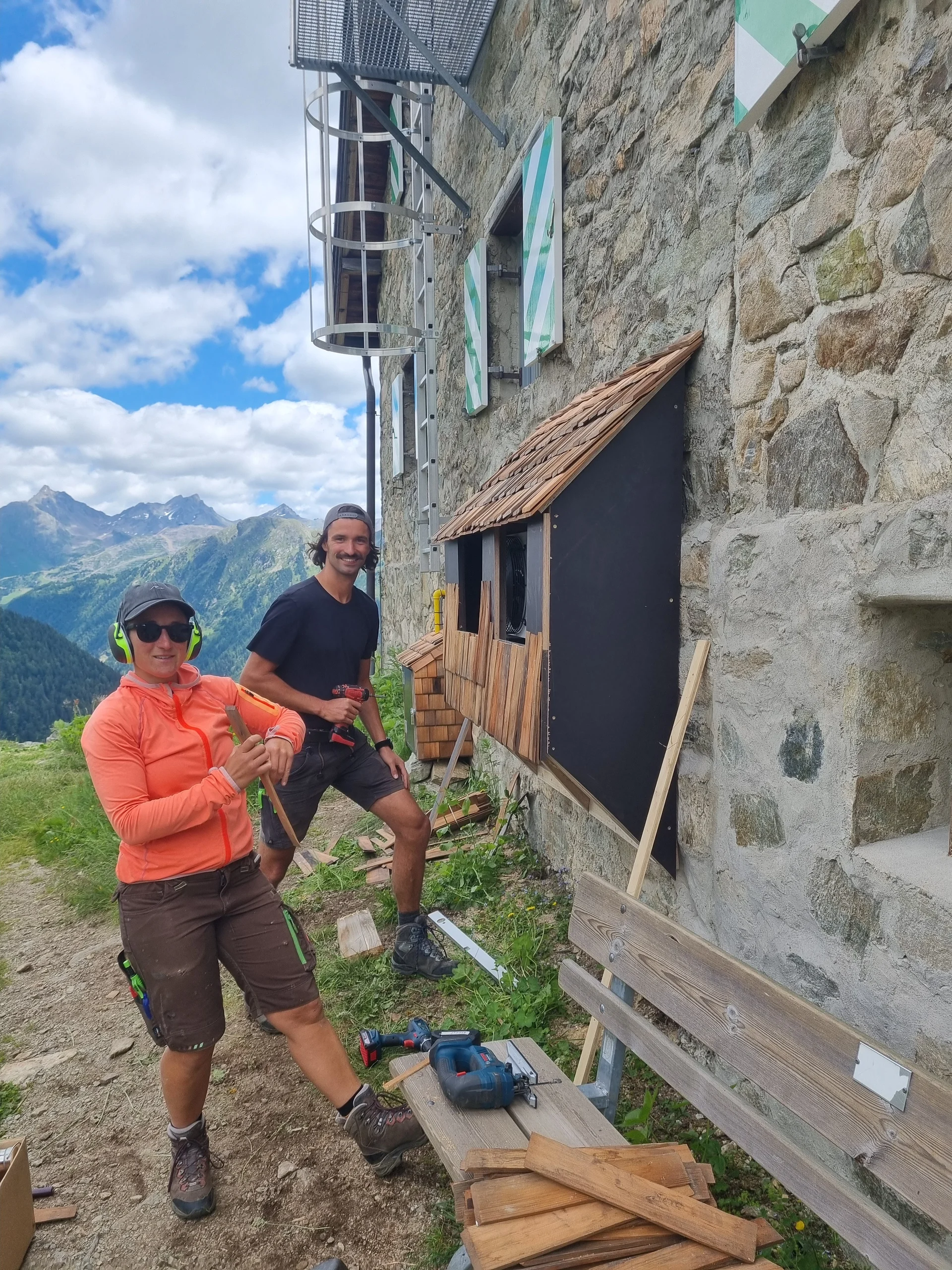 Zwei Personen arbeiten an einer Holzverkleidung an der Aussenwnd der Häfler Hütte, umgeben von Werkzeug und Holzlatten. | © DAV-FN / R. Klees o. R. Zahner
