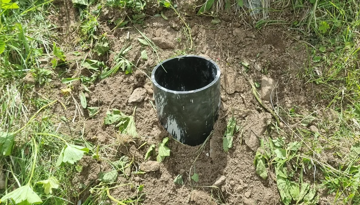 Schwarzes Kunststoffrohr in der Erde, umgeben von Gras und Pflanzen, Teil eines Zaun-Fundaments | © DAV-FN / R. Klees o. R. Zahner