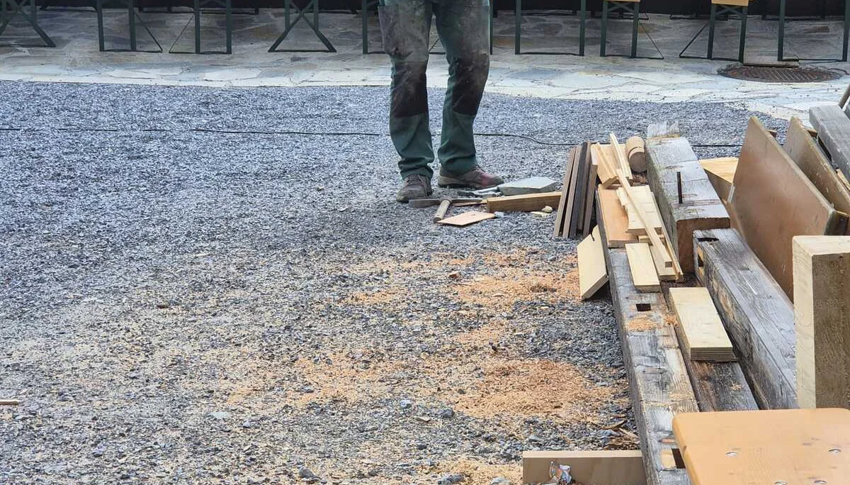 Person in Arbeitskleidung hält eine Motorsäge vor einem Holzstapel im Außenbereich der Häfler Hütte | © DAV-FN / R. Klees o. R. Zahner