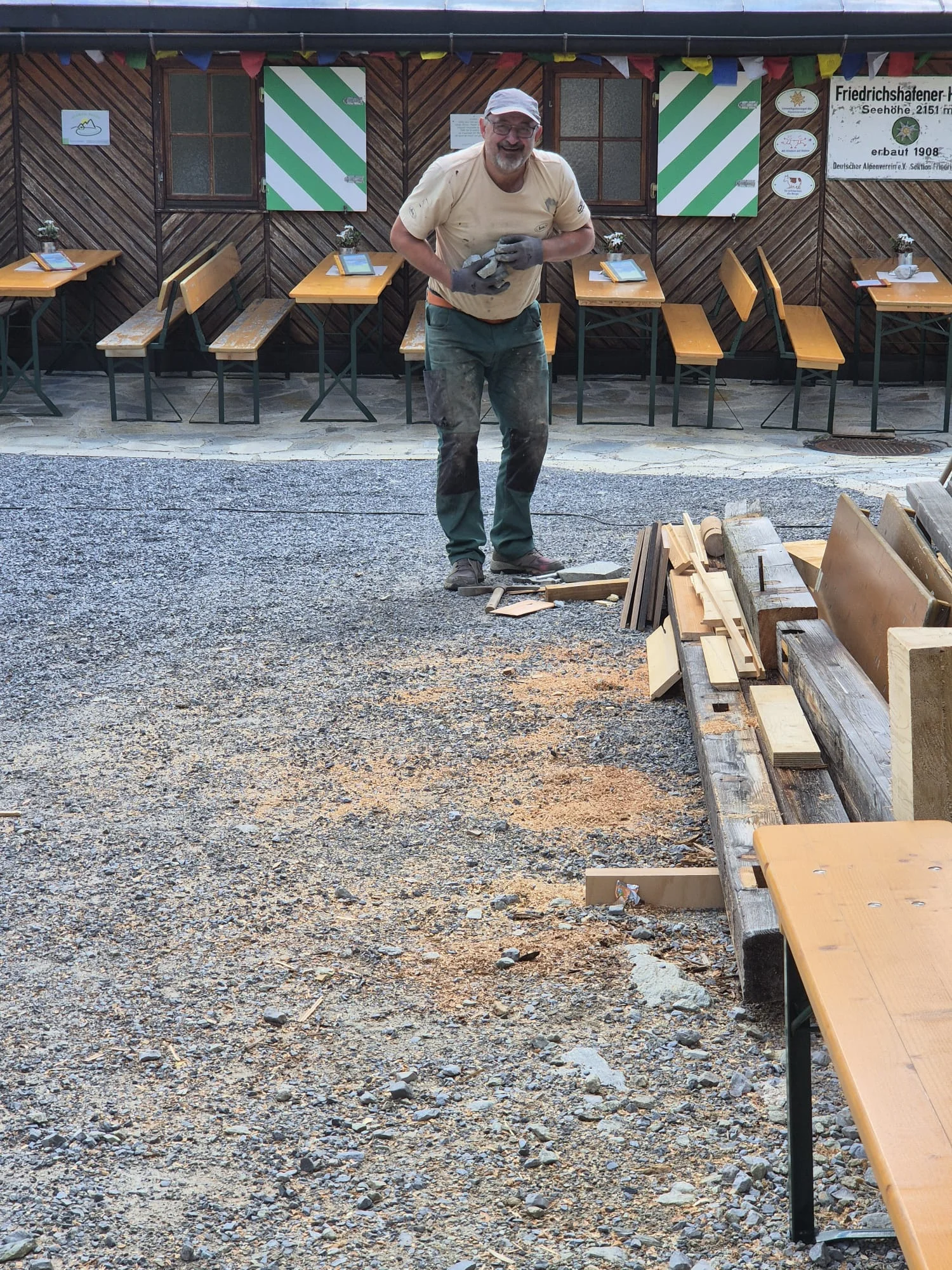 Person in Arbeitskleidung hält eine Motorsäge vor einem Holzstapel im Außenbereich der Häfler Hütte | © DAV-FN / R. Klees o. R. Zahner