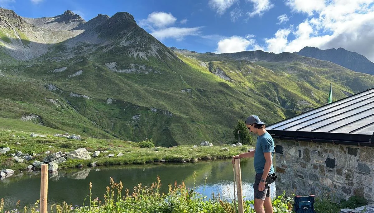 Mann mit Baseballkappe und T-Shirt steht neben einem Anbau der Häfler Hüttet am Bergsee im Verwall | © DAV-FN / R. Klees o. R. Zahner